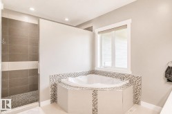 Corner soaking tub with mosaic tile surround, walk-in shower with pebble floor, and a window with a roller shade - 