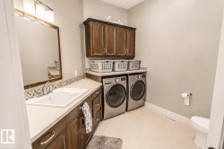 Functional laundry area featuring a built-in countertop with an integrated sink, dark wood-finish cabinetry, a mosaic tile backsplash, and light-toned flooring - 