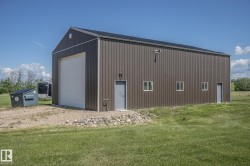 Spacious metal-sided outbuilding featuring a large white roll-up door, multiple windows, two pedestrian entry doors, and a gravel perimeter - 