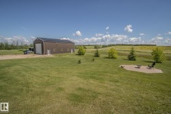 Expansive green lawn with a large brown metal-sided outbuilding featuring a roll-up garage door and multiple entry doors - 