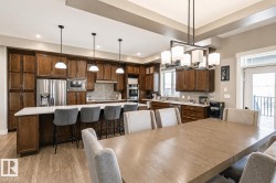 Open-concept kitchen and dining area featuring rich wood cabinetry, stainless steel appliances, a large island with seating, a tile backsplash, and wood-finish flooring - 