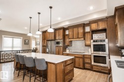 Spacious kitchen featuring an oversized central island with seating, pendant lighting, wood-finish flooring, stainless steel appliances, and ample cabinetry with upper crown molding - 