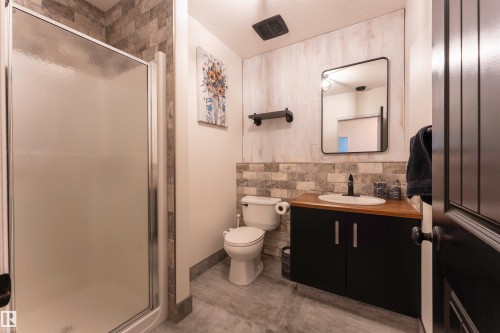 Three-quarter bathroom featuring a framed shower enclosure with frosted glass, a toilet, and a vanity with a wood-finish countertop - 4804 64 Avenue, Cold Lake, AB 
