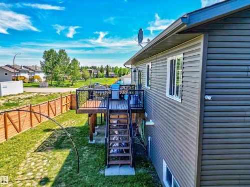 Raised wooden deck with black metal railings, dark grey siding, white-framed windows, and a wooden privacy fence - 4804 64 Avenue, Cold Lake, AB 