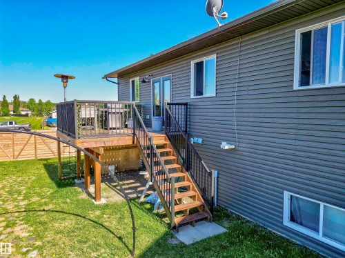 Rear exterior featuring a raised wooden deck with dark railings, a matching wooden staircase with dark metal railings, gray horizontal siding, and multiple white-framed windows - 4804 64 Avenue, Cold Lake, AB 