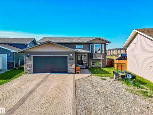 Two-story residence featuring a gray exterior with stone accents, a two-car garage, and a paver driveway - 4804 64 Avenue, Cold Lake, AB 