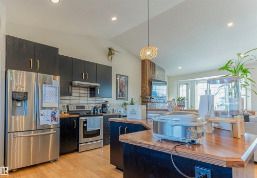 Open-concept kitchen featuring dark wood cabinetry, stainless steel appliances, wood-finish countertops, and light wood-finish flooring - 4804 64 Avenue, Cold Lake, AB 
