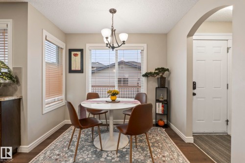 Dining area featuring wood-finish flooring, an arched entryway, two windows with blinds, a built-in cabinet with a granite-style countertop, and an overhead chandelier light fixture - 1542 33A St Nw, Edmonton, AB 