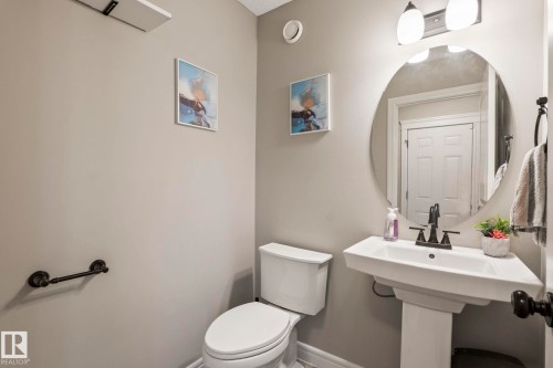 Pedestal sink with a dark bronze faucet, accompanied by a round mirror and a two-light fixture - 1542 33A St Nw, Edmonton, AB 