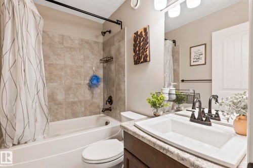 Full bathroom featuring a tub/shower combination with tiled surround, a built-in vanity with a rectangular sink, dark bronze fixtures, and overhead vanity lighting - 1542 33A St Nw, Edmonton, AB 
