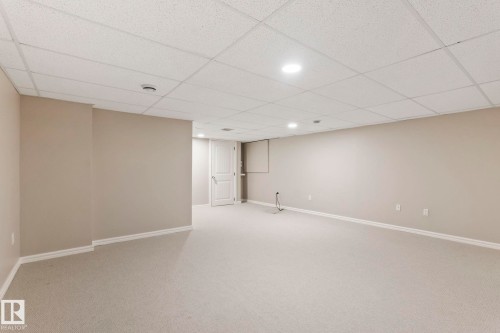 Spacious room featuring neutral carpeting, light beige walls, and a drop ceiling with recessed lighting - 1542 33A St Nw, Edmonton, AB 
