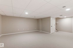 Spacious finished basement featuring light gray carpeting, neutral wall tones, white trim, and a drop ceiling with recessed lighting - 