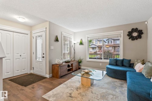 Entryway and living area featuring wood-finish flooring, a white paneled front door with decorative glass inserts, and a closet with bifold doors - 1542 33A St Nw, Edmonton, AB 
