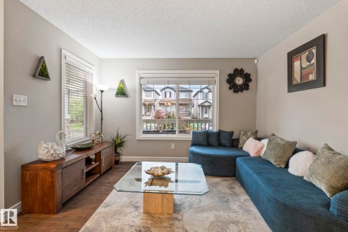 Bright living area featuring wood-finish flooring, two windows with blinds, and neutral wall tones - 1542 33A St Nw, Edmonton, AB 