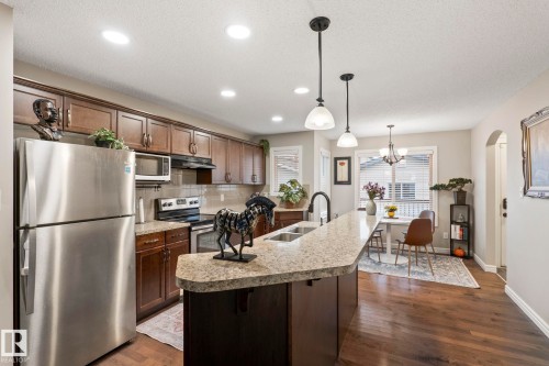 Kitchen featuring a central island with an undermount sink, pendant lighting, stainless steel appliances, wood-finish flooring, and ample cabinetry - 1542 33A St Nw, Edmonton, AB 
