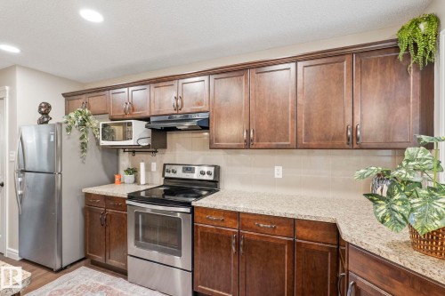 Kitchen featuring extensive wood cabinetry with modern hardware, speckled countertops, and stainless steel appliances - 1542 33A St Nw, Edmonton, AB 