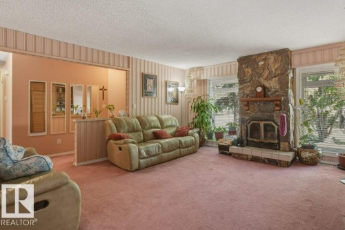 Spacious room featuring a stone fireplace with a raised hearth, large windows with horizontal blinds, textured wall covering, and a carpeted floor - 8901 94 Avenue, Fort Saskatchewan, AB 