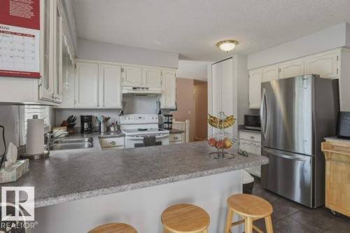 Kitchen featuring white cabinetry, grey countertops, stainless steel refrigerator, white range, and built-in double sink - 8901 94 Avenue, Fort Saskatchewan, AB 