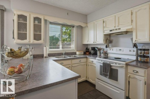 Kitchen featuring cream-colored cabinetry, laminate countertops, and a double basin stainless steel sink - 8901 94 Avenue, Fort Saskatchewan, AB 