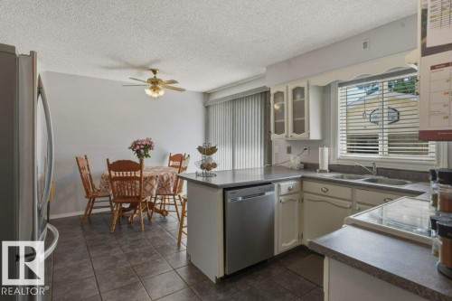 Kitchen featuring tile flooring, white cabinetry, a built-in stainless steel dishwasher, and a double basin sink - 8901 94 Avenue, Fort Saskatchewan, AB 