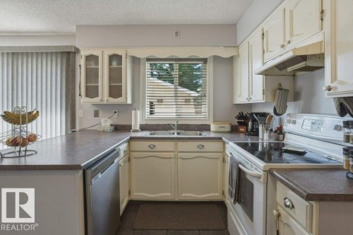 U-shaped kitchen featuring cream cabinetry, a stainless steel dishwasher, and a window above the double basin sink - 8901 94 Avenue, Fort Saskatchewan, AB 