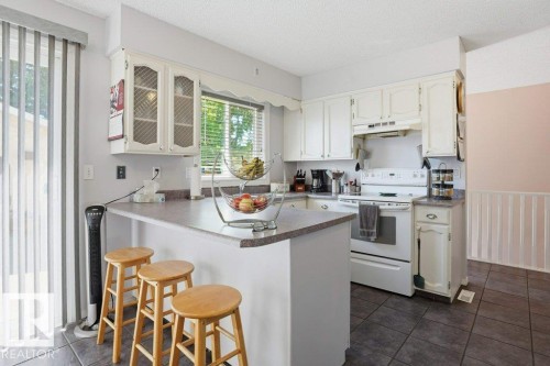 White cabinetry kitchen featuring a peninsula with countertop seating, a complete suite of white appliances, and dark tile flooring - 8901 94 Avenue, Fort Saskatchewan, AB 