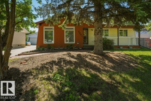 Exterior showcasing horizontal siding in two tones, a front porch with white railing, a mature tree, an asphalt driveway, and a manicured lawn - 8901 94 Avenue, Fort Saskatchewan, AB 