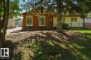 Exterior showcasing horizontal siding in two tones, a front porch with white railing, a mature tree, an asphalt driveway, and a manicured lawn - 8901 94 Avenue, Fort Saskatchewan, AB 