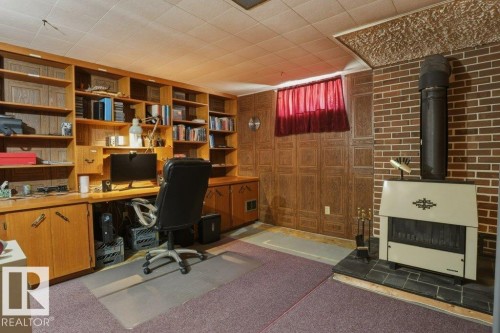 Built-in wood-finish shelving and desk system, brick accent wall with a fireplace, textured ceiling paneling, and wall-to-wall carpeting - 8901 94 Avenue, Fort Saskatchewan, AB 