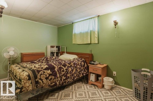 Bedroom featuring green painted walls, a window with light-filtering curtains, a drop ceiling, and a wall-mounted sconce - 8901 94 Avenue, Fort Saskatchewan, AB 