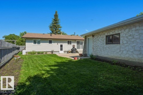 Expansive grassy backyard featuring a paved patio, perimeter fencing, and a detached structure with a single window and door - 8901 94 Avenue, Fort Saskatchewan, AB 