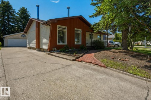 Exterior features include a two-tone facade with wood-look siding and light-colored panels, a concrete driveway, an attached garage, a red brick pathway, and mature trees - 8901 94 Avenue, Fort Saskatchewan, AB 