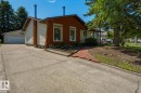 Exterior features include a two-tone facade with wood-look siding and light-colored panels, a concrete driveway, an attached garage, a red brick pathway, and mature trees - 8901 94 Avenue, Fort Saskatchewan, AB 