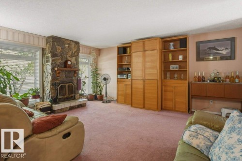 Living area featuring a stone-clad fireplace with a raised hearth, broad windows with horizontal blinds, and extensive built-in wooden cabinetry - 8901 94 Avenue, Fort Saskatchewan, AB 