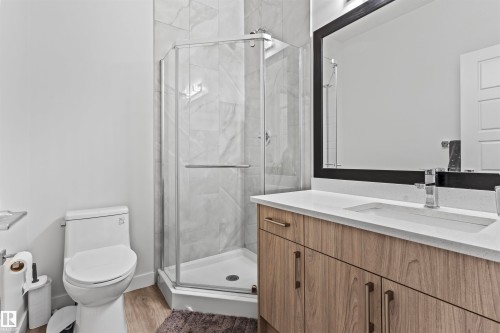 Bathroom featuring a glass-enclosed corner shower with marble-look tile surround, a single vanity with wood-finish cabinetry, a white countertop, and an integrated rectangular sink - 8046 Kiriak Link, Edmonton, AB - Indoor Photo Showing Bathroom