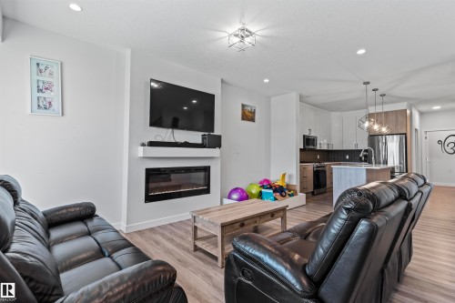 Open-concept living space featuring wood-finish flooring, recessed lighting, and a contemporary fireplace with a mounted television above - 8046 Kiriak Link, Edmonton, AB - Indoor Photo Showing Living Room With Fireplace