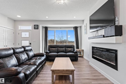 Living area featuring light wood-finish flooring, recessed lighting, and a wide window with dark drapery - 8046 Kiriak Link, Edmonton, AB - Indoor Photo Showing Living Room With Fireplace