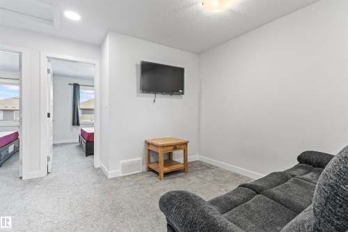 Carpeted room with a wall-mounted television and a light wood-finish side table - 8046 Kiriak Link, Edmonton, AB - Indoor