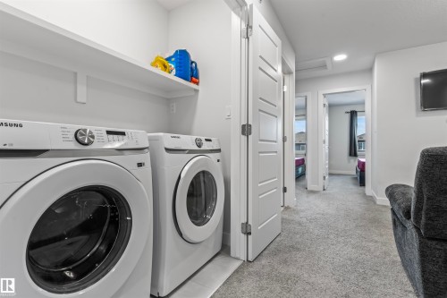 Dedicated laundry area with built-in shelving, two white front-loading appliances, and light grey wall paint - 8046 Kiriak Link, Edmonton, AB - Indoor Photo Showing Laundry Room