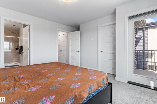 Bedroom featuring a glass-enclosed shower, light grey carpeting, white trim, and a patio door leading to a balcony with black metal railings - 8046 Kiriak Link, Edmonton, AB - Indoor Photo Showing Bedroom