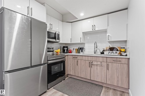 Contemporary kitchen featuring white upper cabinetry, wood-finish lower cabinetry, and stainless steel appliances - 8046 Kiriak Link, Edmonton, AB - Indoor Photo Showing Kitchen With Upgraded Kitchen
