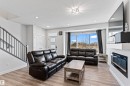 Bright living area featuring wood-finish flooring, a contemporary electric fireplace with a white mantel, and a prominent bay window - 8046 Kiriak Link, Edmonton, AB  - Indoor Photo Showing Living Room With Fireplace 