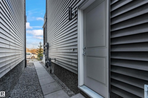 Exterior entry featuring a light gray door with panel detailing, dark gray horizontal siding, and a matte black wall-mounted light fixture - 8046 Kiriak Link, Edmonton, AB - Outdoor With Exterior