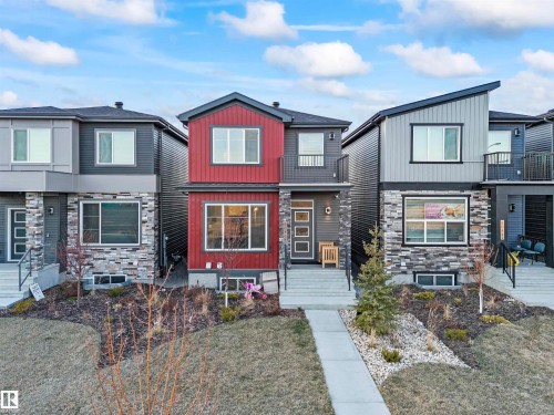 Modern exterior featuring red and gray siding, stone accents, a second-story balcony, and a paved walkway leading to the entrance - 8046 Kiriak Link, Edmonton, AB - Outdoor With Facade