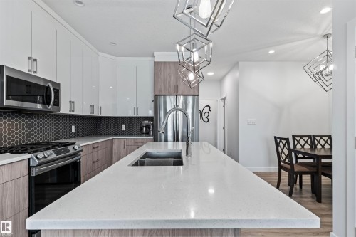 Contemporary kitchen featuring a large center island with an undermount sink, white countertops, and a dark hexagonal tile backsplash - 8046 Kiriak Link, Edmonton, AB - Indoor Photo Showing Kitchen With Double Sink With Upgraded Kitchen