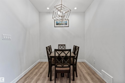 Recessed dining area featuring light wood-finish flooring, white baseboards, and a contemporary geometric chandelier - 8046 Kiriak Link, Edmonton, AB - Indoor Photo Showing Dining Room