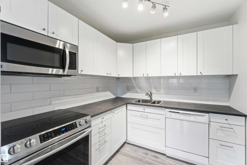 Modern kitchen featuring white cabinetry, dark countertops, a stainless steel over-the-range microwave, and a stainless steel electric range - 3312 106 Avenue, Edmonton, AB 