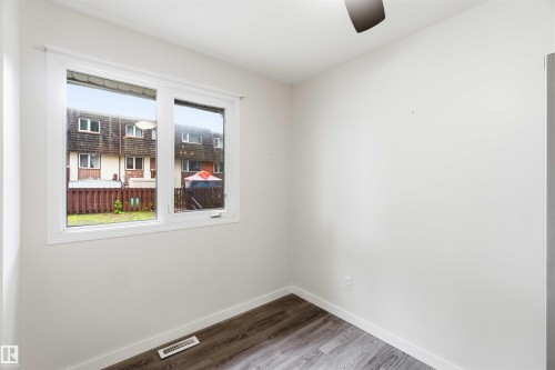 Interior space featuring a white framed window, wood-finish flooring, white walls, and a ceiling fan - 3312 106 Avenue, Edmonton, AB 