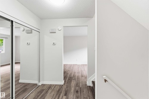 Entryway featuring wood-finish flooring, a mirrored closet with sliding doors, white baseboards, and a simple wall-mounted handrail leading to an upper level - 3312 106 Avenue, Edmonton, AB 