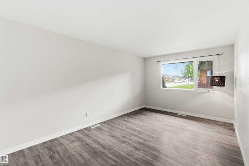 Bright interior space featuring a large window, light-toned walls, and wood-finish flooring - 3312 106 Avenue, Edmonton, AB 